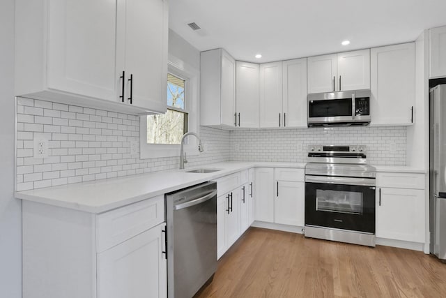 kitchen with visible vents, a sink, stainless steel appliances, white cabinets, and light wood-type flooring