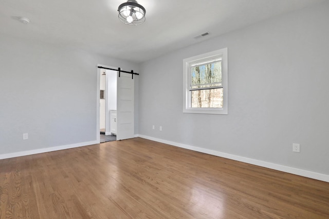 unfurnished room featuring a barn door, baseboards, visible vents, and wood finished floors