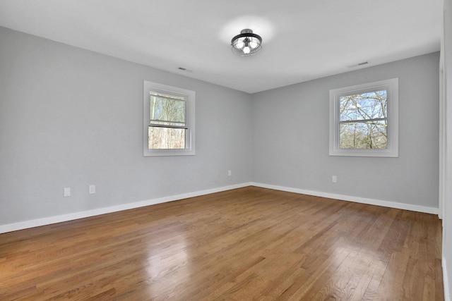 empty room with baseboards, plenty of natural light, visible vents, and wood finished floors