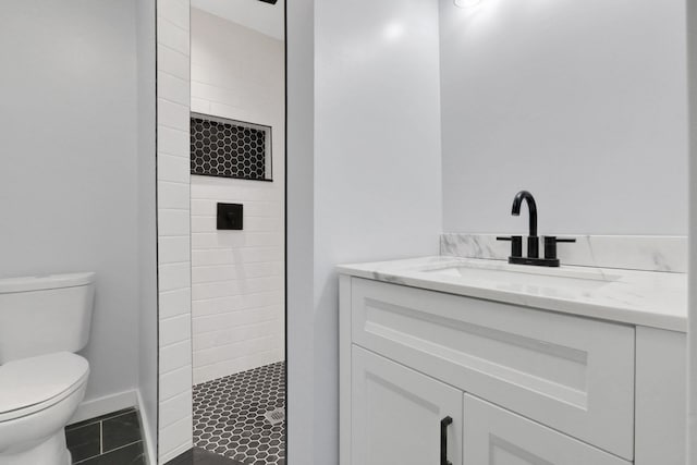 full bathroom with baseboards, tiled shower, toilet, and vanity