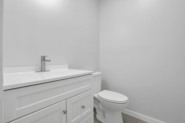 half bathroom with toilet, vanity, and baseboards