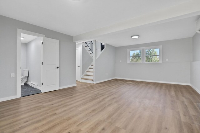 basement featuring stairway, light wood-style flooring, baseboards, and baseboard heating