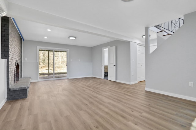 unfurnished living room with an AC wall unit, stairway, light wood finished floors, baseboards, and a brick fireplace