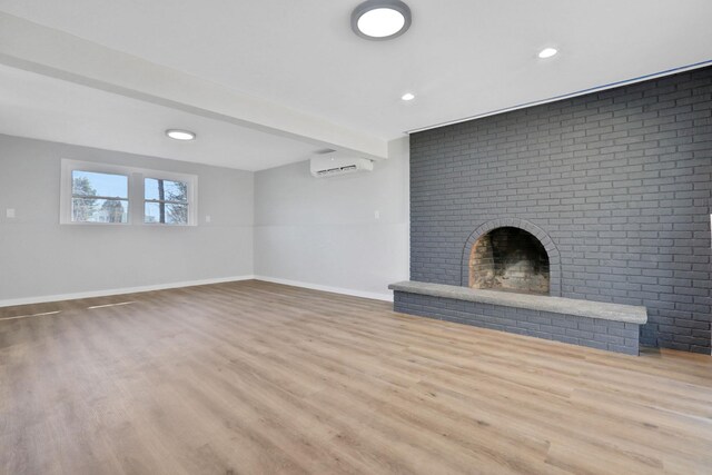 unfurnished living room featuring baseboards, beamed ceiling, an AC wall unit, a fireplace, and wood finished floors