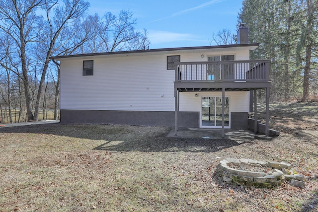 back of house featuring a wooden deck, a fire pit, a chimney, and a patio area