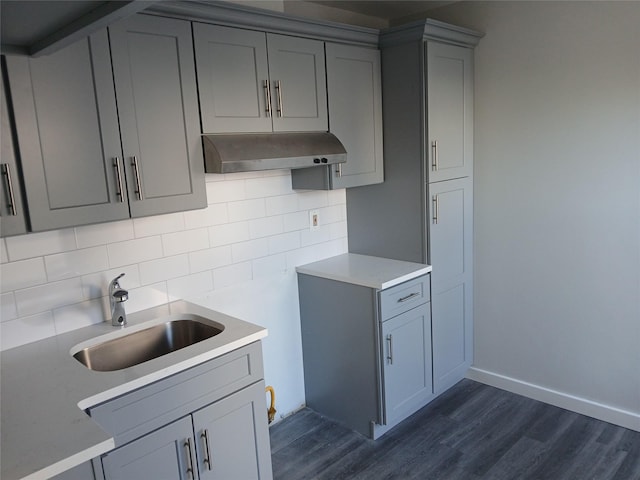 kitchen with gray cabinetry, dark wood-type flooring, a sink, ventilation hood, and backsplash