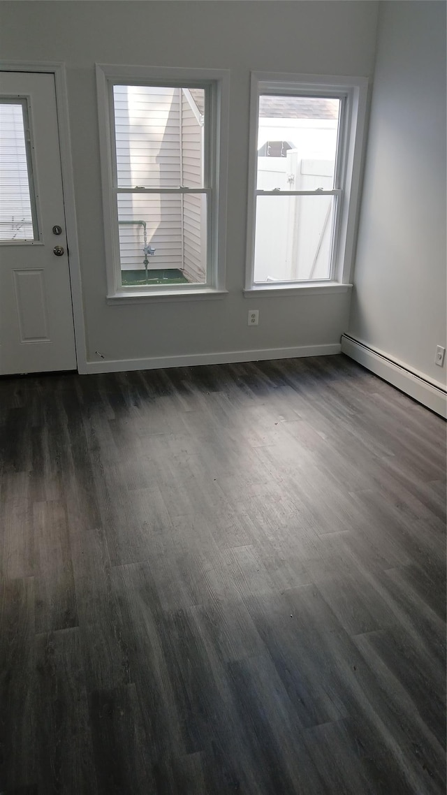 empty room with dark wood-type flooring, a baseboard radiator, and baseboards