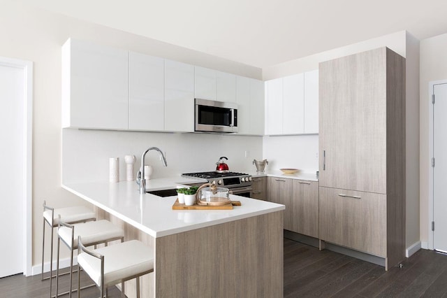 kitchen featuring a breakfast bar, light countertops, appliances with stainless steel finishes, modern cabinets, and a peninsula