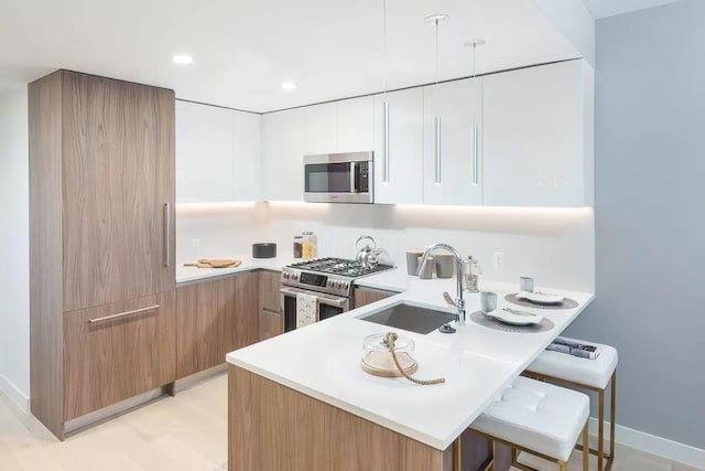 kitchen with a breakfast bar area, a peninsula, a sink, appliances with stainless steel finishes, and modern cabinets