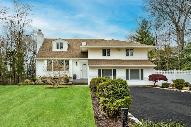 split level home with roof with shingles, a chimney, fence, and a front yard