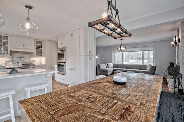 kitchen featuring stainless steel double oven, white cabinets, light countertops, backsplash, and glass insert cabinets