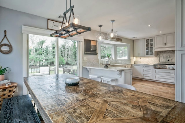 kitchen with stainless steel gas cooktop, a breakfast bar, white cabinetry, decorative backsplash, and glass insert cabinets