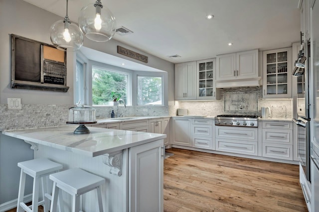 kitchen with a peninsula, a sink, visible vents, glass insert cabinets, and stainless steel gas stovetop