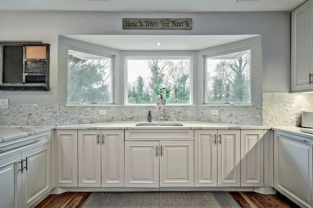 kitchen with dark wood-style floors, tasteful backsplash, light stone counters, and a sink