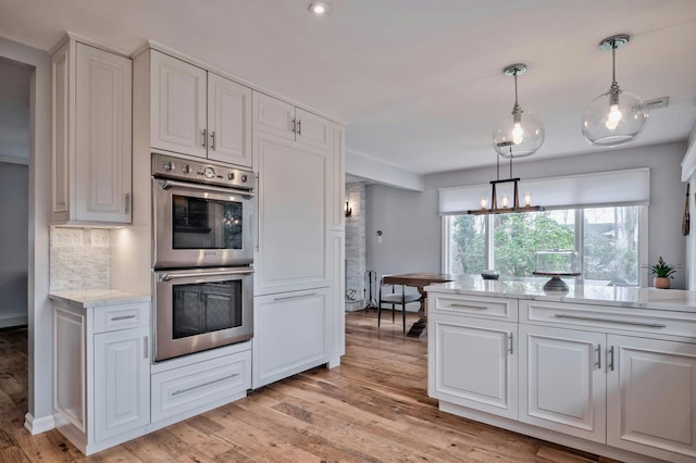 kitchen with stainless steel double oven, backsplash, white cabinetry, and light wood-style floors