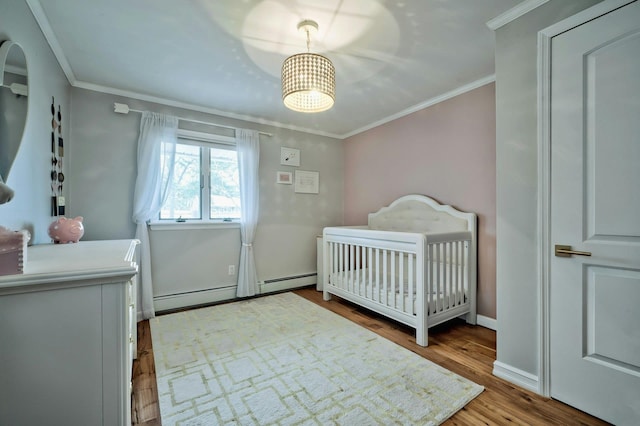 bedroom featuring a crib, baseboards, crown molding, and wood finished floors