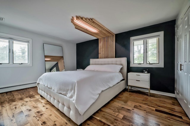 bedroom featuring a closet, multiple windows, baseboard heating, and hardwood / wood-style floors