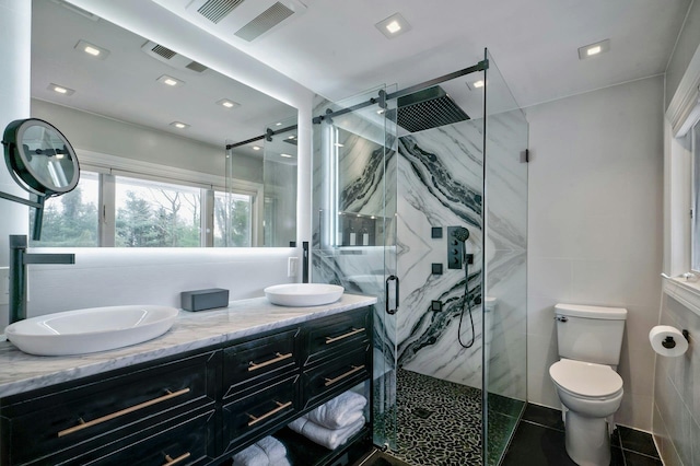 full bath with double vanity, a marble finish shower, toilet, and a sink