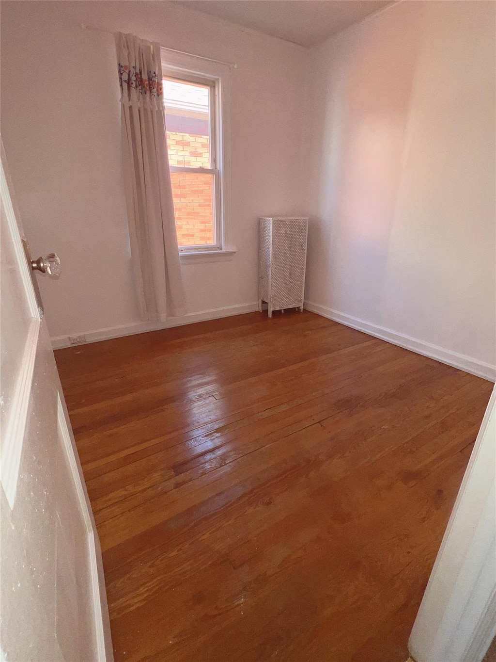 unfurnished room featuring radiator, baseboards, and wood finished floors