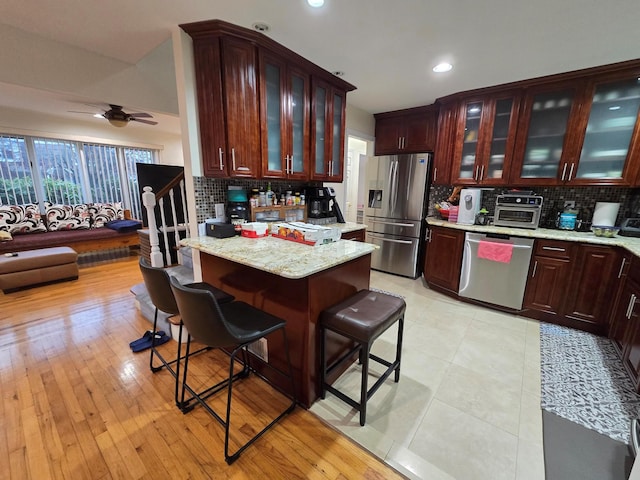 kitchen featuring a toaster, a breakfast bar area, stainless steel appliances, tasteful backsplash, and a ceiling fan