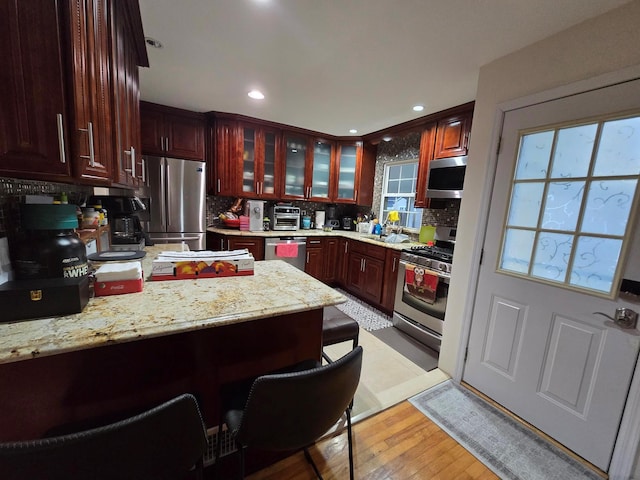 kitchen featuring appliances with stainless steel finishes, light wood-style floors, glass insert cabinets, and decorative backsplash