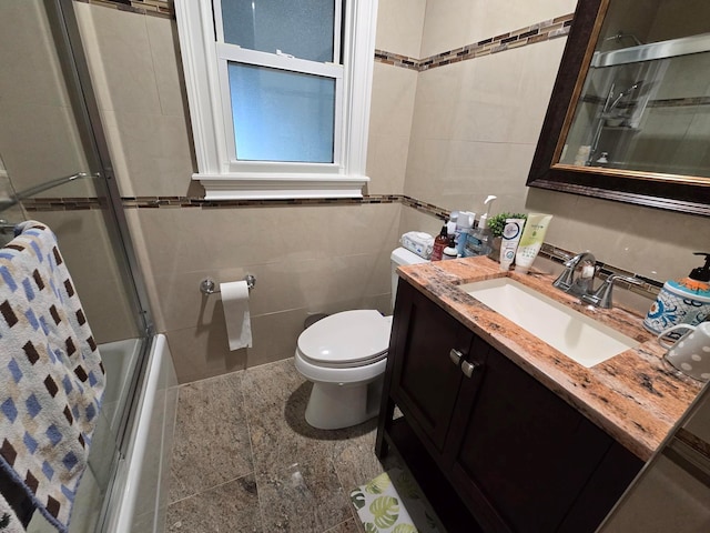 full bathroom featuring vanity, tile walls, toilet, and bath / shower combo with glass door