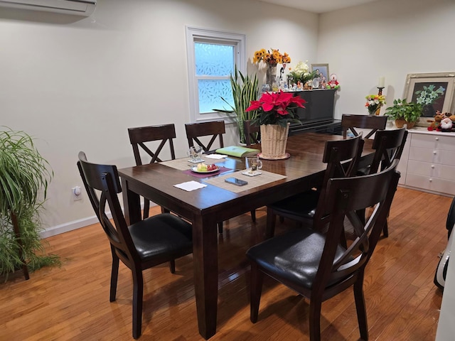 dining space featuring a wall unit AC, light wood finished floors, and baseboards