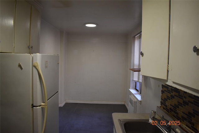 kitchen featuring a sink, white cabinetry, baseboards, freestanding refrigerator, and radiator