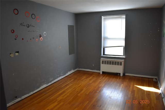 empty room featuring baseboards, hardwood / wood-style floors, and radiator