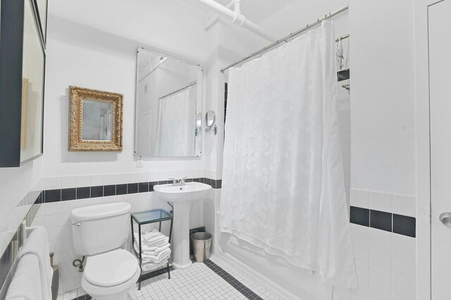 bathroom featuring a wainscoted wall, a sink, tile patterned flooring, tile walls, and toilet