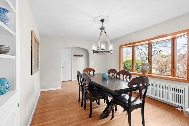 dining space with radiator, baseboards, light wood-style flooring, arched walkways, and a notable chandelier