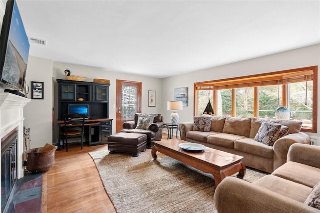 living area featuring light wood-type flooring, visible vents, and a fireplace with flush hearth