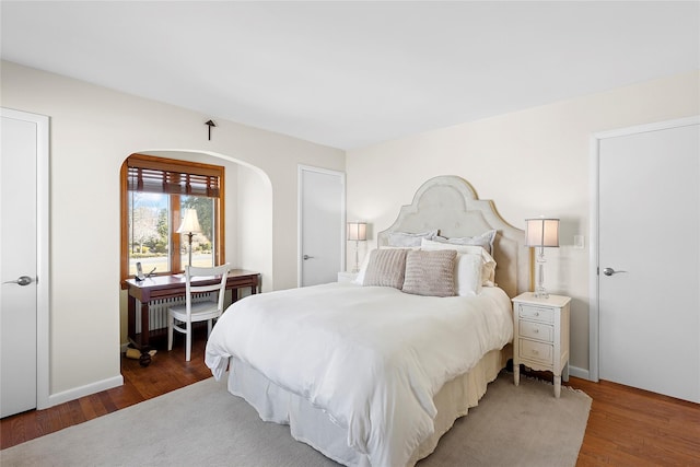 bedroom featuring arched walkways and wood finished floors