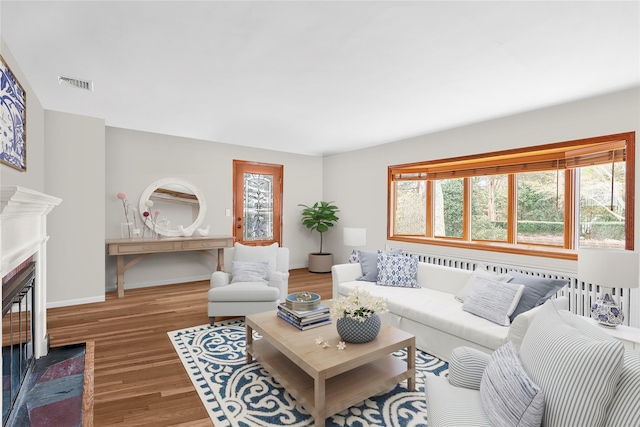 living room with a fireplace with flush hearth, baseboards, wood finished floors, and visible vents