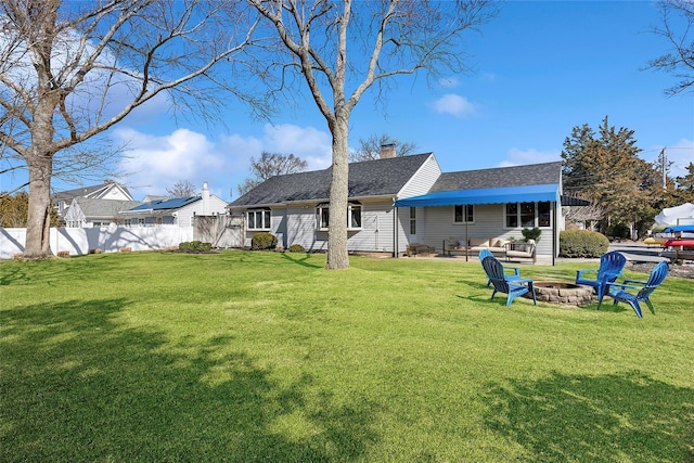 rear view of house with a chimney, fence, a shingled roof, a yard, and an outdoor living space with a fire pit