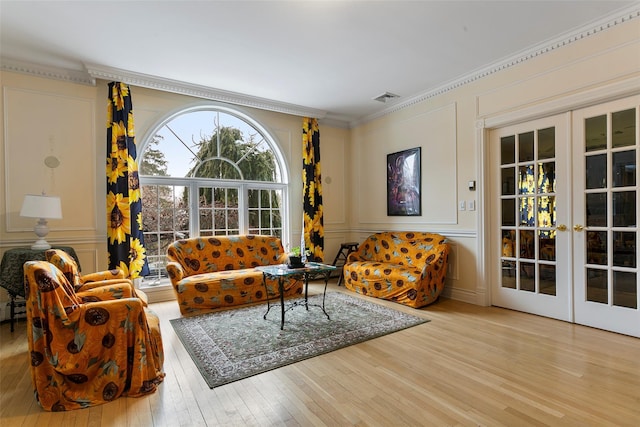 living area featuring a decorative wall, french doors, crown molding, and wood-type flooring