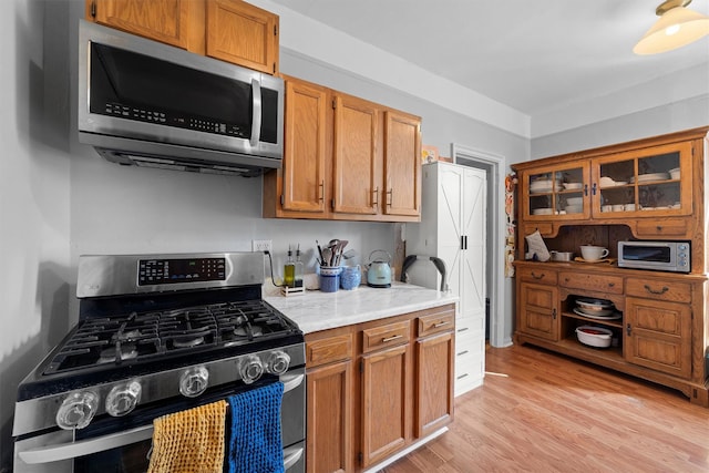 kitchen featuring appliances with stainless steel finishes, light wood-type flooring, and brown cabinets