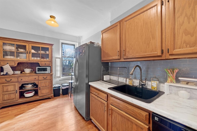 kitchen featuring light wood-style flooring, stainless steel appliances, a sink, light countertops, and backsplash