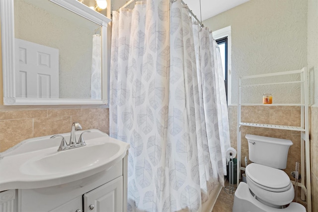 full bathroom with a wainscoted wall, tile walls, toilet, and vanity