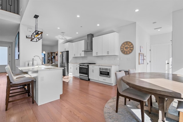 kitchen with light wood finished floors, wall chimney exhaust hood, a peninsula, and appliances with stainless steel finishes