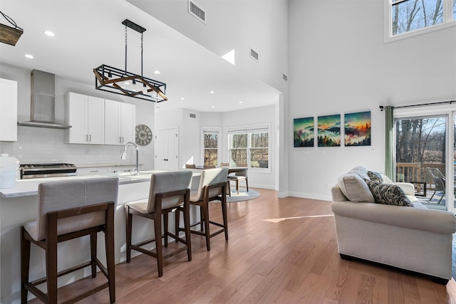 kitchen with visible vents, wall chimney range hood, light countertops, light wood-style floors, and white cabinets