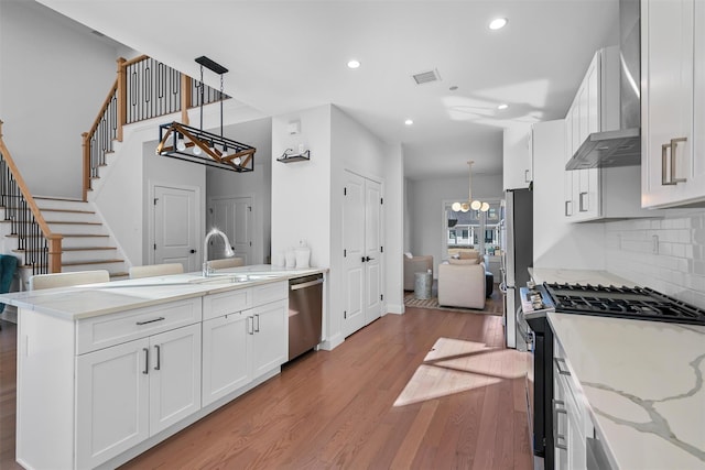 kitchen with a peninsula, a sink, stainless steel appliances, a notable chandelier, and light wood-type flooring