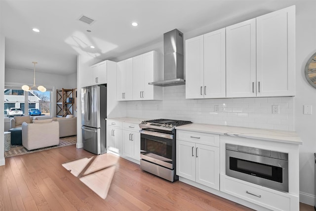 kitchen featuring light stone countertops, visible vents, light wood finished floors, appliances with stainless steel finishes, and wall chimney exhaust hood