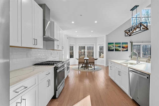 kitchen with decorative backsplash, light wood-style flooring, stainless steel appliances, wall chimney exhaust hood, and a sink