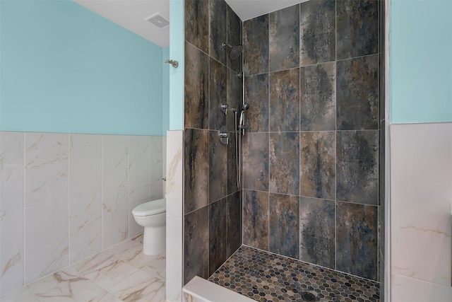 full bathroom with visible vents, tiled shower, tile walls, toilet, and marble finish floor