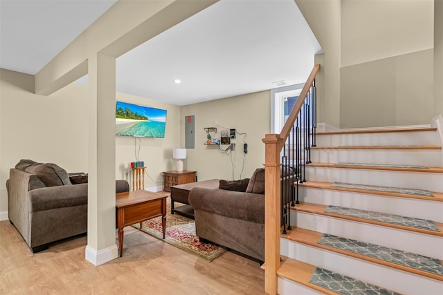 living area with wood finished floors, baseboards, electric panel, recessed lighting, and stairs