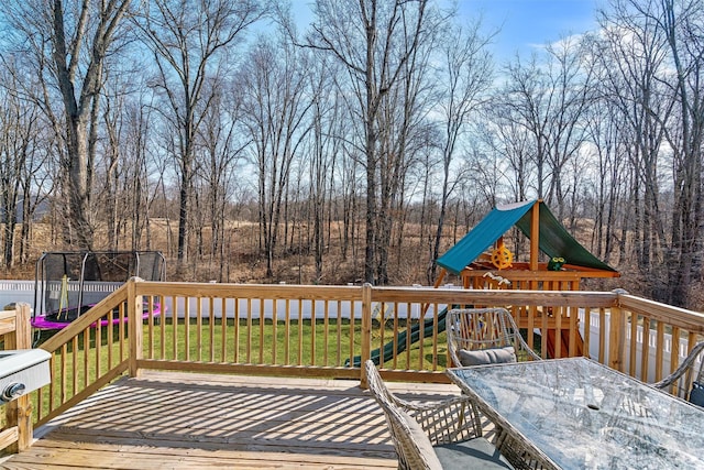 deck with outdoor dining area, a yard, and a trampoline