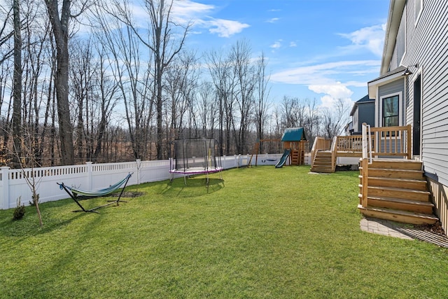 view of yard with a fenced backyard, a wooden deck, a playground, and a trampoline