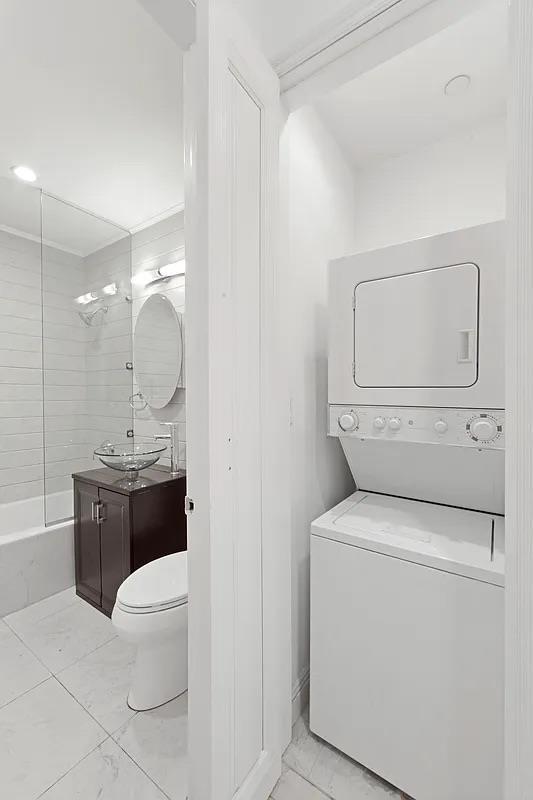 full bathroom featuring toilet, marble finish floor, stacked washer / drying machine, and vanity