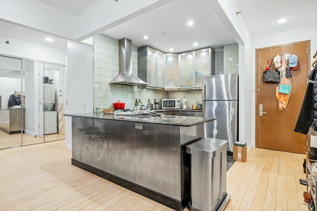 kitchen featuring stacked washer and dryer, wall chimney exhaust hood, light wood-style flooring, and freestanding refrigerator